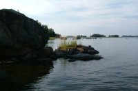 A big boulder in the water with islands in the background.